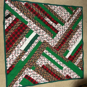 May include: A green, red, and white patchwork quilt with a geometric pattern. The quilt is made of different fabrics, including plaid, floral, and solid colors.