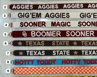 May include: A selection of beaded lanyards with different text and designs. The lanyards display phrases such as "GIG'EM AGGIES", "SOONER MAGIC", and "HOTTY TODDY". Colours include white, maroon, black, gold, blue, orange, and yellow.
