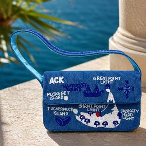 May include: A blue beaded handbag featuring a map design with white text labels including ACK, Muskeget Island, Tuckernuck Island, Great Point Light, Brant Point Light, and Sankaty Head Light, along with a compass rose and a sailboat illustration.