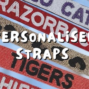 May include: Close-up of several beaded straps with text, including "RAZORBACKS", "CATS", and "TIGERS". The straps are in various colors, such as red, tan, and white. The words "PERSONALISED STRAPS" are in the center.