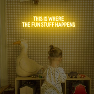 Op de afbeelding: Een geel neon-bord met de tekst "This is where the fun stuff happens" op een gele en witte gingham-achtergrond. Een kind staat voor het bord.