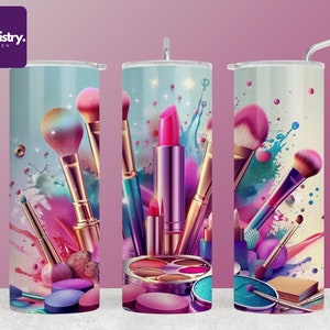 May include: A set of three stainless steel tumblers featuring a colourful design of makeup brushes, lipstick and eyeshadow palettes. The tumblers have a white background with pink, blue and green splashes of paint.
