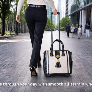 Pu&ograve; includere: Una borsa tote con ruote, con manico e ruote nere, viene trascinata lungo un vialetto pavimentato. La borsa &egrave; color crema con dettagli neri e un nappa decorativa. Il testo "Glide through your day with smooth all-terrain wheels!" &egrave; in basso.