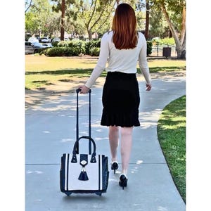 Pu&ograve; includere: Una borsa tote con ruote con un design in bianco e nero, un manico nero e un nappa nera. La borsa viene trascinata lungo un vialetto pavimentato.