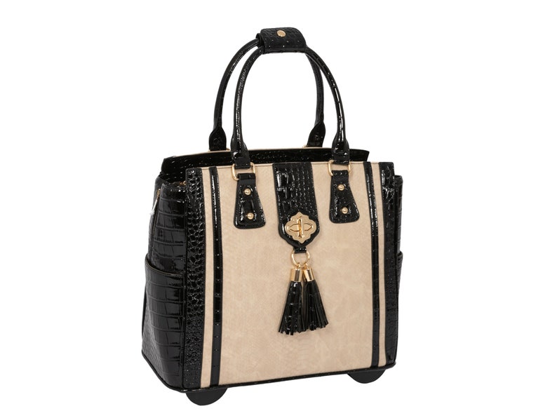A cream and black rolling laptop bags made with faux leather in alligator and python embossed fabric.The bag has gold accent hardware and black patent tassels. The stylish design of the laptop tote makes it a fashionable and functional bag for work, travel, shopping, or everyday errands.
