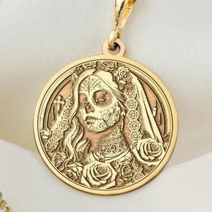 Puede incluir: Un collar de oro con un colgante redondo que presenta una imagen detallada de una mujer con un diseño de maquillaje de calavera de azúcar. El colgante está rodeado de un diseño floral.