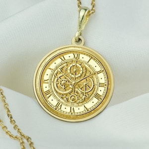 Könnte beinhalten: Eine goldene Halskette mit einem runden Anhänger, der ein detailliertes Zifferblatt zeigt.