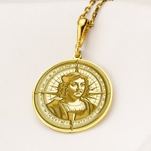 Op de afbeelding: Een gouden kompas hanger ketting met een gedetailleerd beeld van een mannengezicht in het midden. Het kompas heeft een traditioneel ontwerp met windrichtingen en een kompasroos.