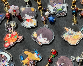 May include: A collection of colorful acrylic charms featuring anime-style illustrations. The charms have gold-colored chains and decorative beads. The designs include cartoon characters, food, and a yellow airplane. The background is a dark, solid color.