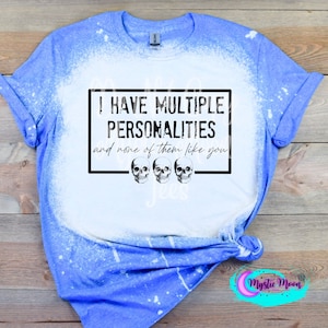 May include: A blue bleached t-shirt with a black and white graphic that says "I have multiple personalities and none of them like you" with three skull images below the text.