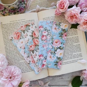 May include: Three floral bookmark designs with pink and white roses on a blue background. The bookmarks are laying on an open book with text about the mutiny on the bounty.