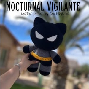 Puede incluir: Un juguete de ganchillo hecho a mano con forma de personaje de murci&eacute;lago negro con ojos blancos y un cintur&oacute;n amarillo. El texto "NOCTURNAL VIGILANTE" y "Crochet pattern by CraftsByErika_" se muestra en la parte superior de la imagen.