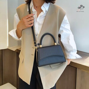 May include: A black faux leather handbag with a gold top handle and a gold chain strap. The bag has a crocodile embossed pattern.