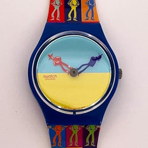 May include: A Swatch Swiss watch with a blue case and a colourful strap. The watch face has a blue and yellow background with two figures. The strap has a repeating pattern of figures in various colours.
