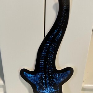 May include: A blue and black whale shark sticker with a white outline. The sticker is on a white surface.