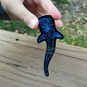 May include: A blue whale shark sticker with a black background. The sticker is covered in white dots.