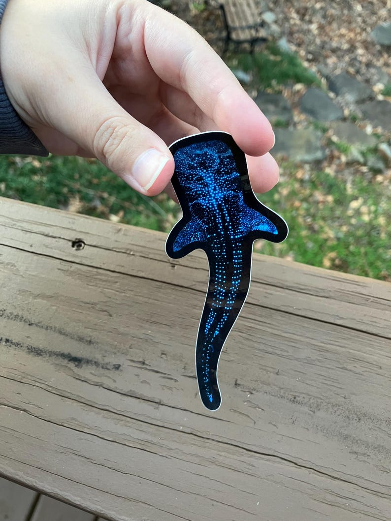 May include: A blue whale shark sticker with a black background. The sticker is covered in white dots.