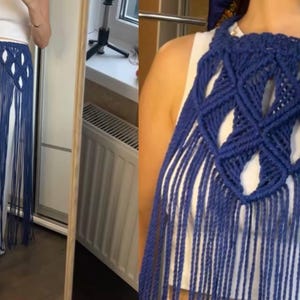 May include: A dark blue macrame accessory featuring an intricate diamond-shaped knotted pattern with long, flowing fringe. The piece is designed to be worn over a white top, creating a layered look with its textured cord construction and open weave.