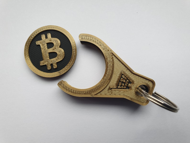 May include: A gold-colored keychain with a Bitcoin symbol on one end and a ring on the other. The Bitcoin symbol is black and white.