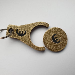 May include: Gold-colored keychain with a coin-shaped charm. Both the keychain and charm have a textured surface and feature a black euro symbol.