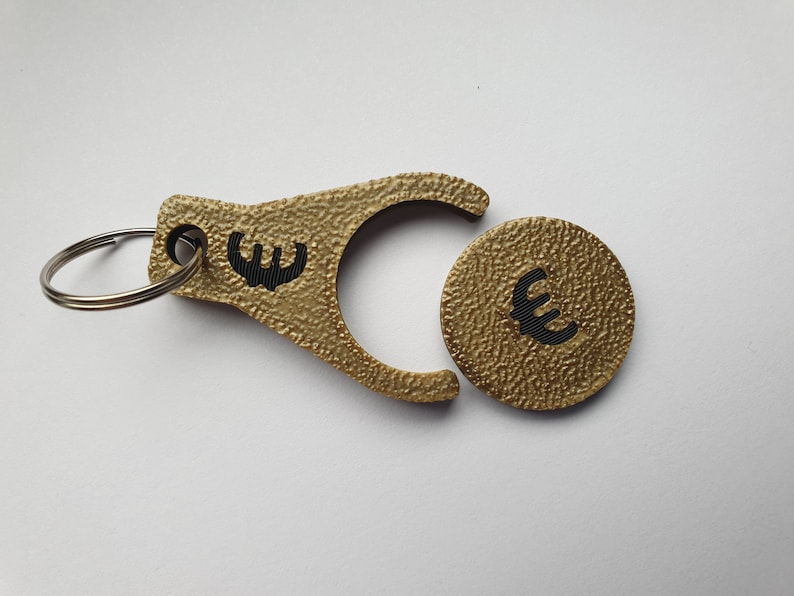 May include: Gold-colored keychain with a coin-shaped charm. Both the keychain and charm have a textured surface and feature a black euro symbol.