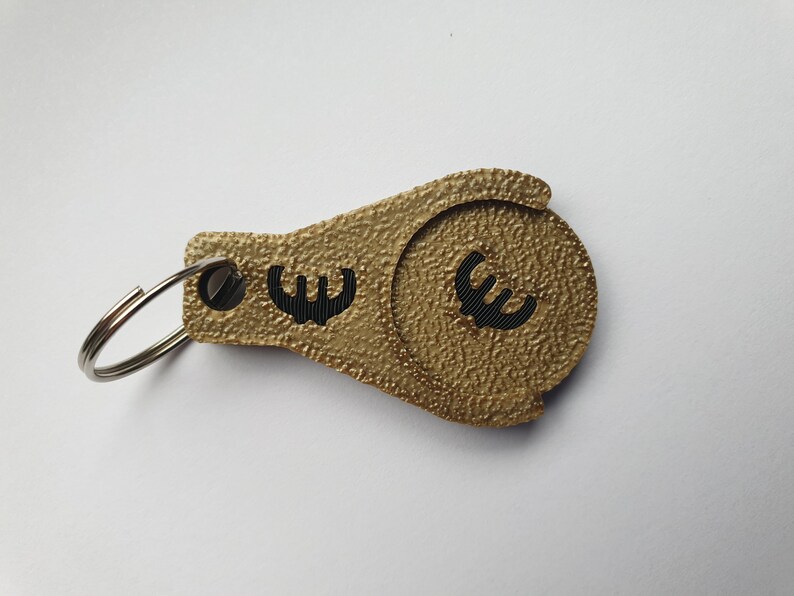 May include: Gold-colored keychain with a coin holder featuring a black euro symbol. The keychain has a silver ring.