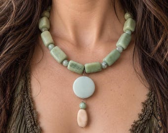 May include: A necklace featuring a series of rectangular light green stone beads interspersed with small round beads. A central pendant consists of a smooth, pale blue circular disc suspended above a smaller, oval-shaped light peach-colored stone bead.