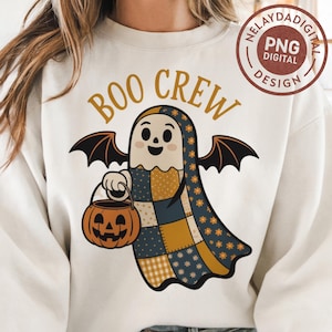 May include: A white sweatshirt featuring a Halloween-themed graphic. The design includes a patchwork ghost holding a jack-o'-lantern bucket, with the words "BOO CREW" in gold lettering above. The ghost has bat wings.