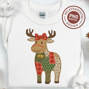 May include: White sweatshirt with a patchwork reindeer design. The reindeer has brown antlers, a red bow, and a body made of various patterned fabrics. Gold bells hang from its neck. The design includes the text "NELAYDADIGITAL PNG DESIGN".