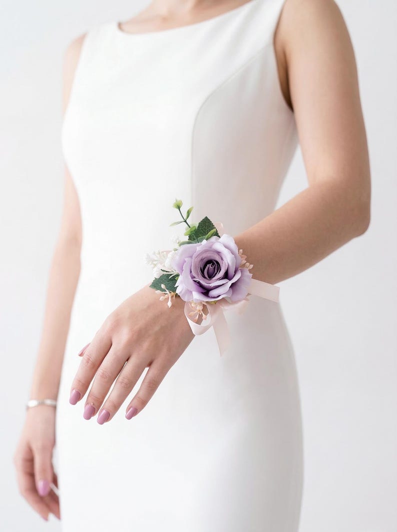 K&ouml;nnte beinhalten: Ein lila Rosen-Handgelenk-Corsage mit Gr&uuml;n und einem hellrosa Band. Das Blumengesteck wird mit einem zarten Band am Handgelenk befestigt, perfekt f&uuml;r Hochzeiten, Abschlussb&auml;lle oder besondere Anl&auml;sse.