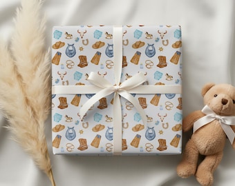 May include: A square gift box wrapped in white paper featuring a repeating pattern of watercolor illustrations including brown cowboy boots, tan hats, blue baby bibs, horses, lassos, and cow skulls, tied with a white satin ribbon.