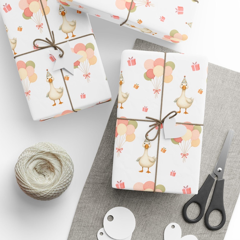 May include: White gift wrap with a repeating pattern of a goose wearing a party hat, balloons, and gift boxes. The gifts are tied with brown twine and a white tag. A ball of twine, scissors, and blank tags are also visible.