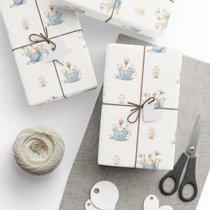 May include: Gift-wrapped presents with a whimsical duckling and teacup pattern. The white paper is tied with brown twine and adorned with a star-shaped tag. A ball of twine, scissors, and blank tags are also visible.