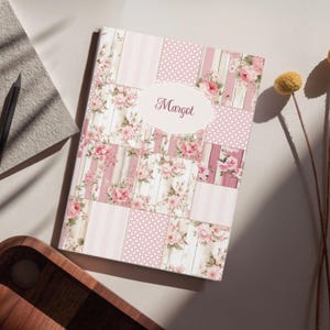 Op de afbeelding: Een notitieboek met een bloemmotief en patchwork-ontwerp. De kaft heeft roze rozen, strepen en panelen met houtlook. De naam "Margot" staat in sierlijke letters op een ovaal.