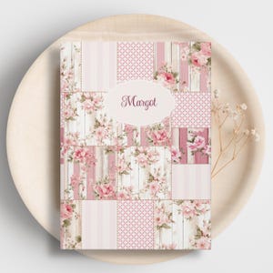 Puede incluir: Un cuaderno con un diseño de patchwork floral con rosas rosas, vetas de madera y patrones geométricos. El nombre "Margot" se muestra en un óvalo. El cuaderno está sobre una bandeja de madera clara.