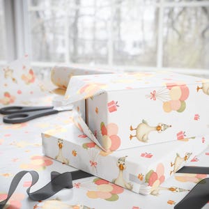 May include: White gift boxes wrapped in patterned paper featuring cartoon geese with party hats, balloons, and gift boxes. A roll of matching wrapping paper and scissors are visible. A black ribbon is in the foreground.