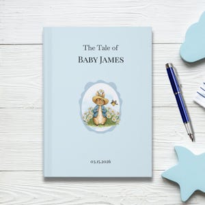 Peut inclure: Un livre à couverture rigide bleu clair intitulé "The Tale of BABY JAMES". La couverture présente une illustration d'un lapin en veste bleue et chapeau de paille, entouré de marguerites. La date 03.15.2026 est imprimée en bas.