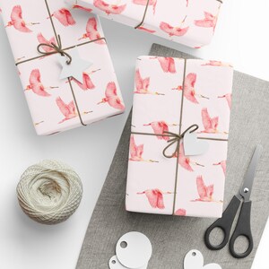 May include: Pink and white wrapping paper with a repeating pattern of pink roseate spoonbills. The paper is wrapped around a gift box with a brown twine bow and a white star-shaped gift tag.