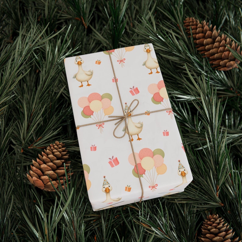 May include: A wrapped gift with a white background featuring a pattern of cartoon geese wearing party hats, balloons, and gift boxes. The gift is tied with twine and set against a backdrop of pine needles and pine cones.