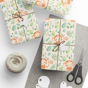 Puede incluir: Tres hojas de papel de regalo con un patrón de monos y hojas verdes sobre un fondo crema. El papel está atado con cuerda y tiene una estrella blanca y una etiqueta en forma de corazón.
