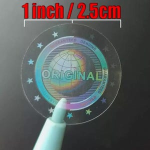 Peut inclure: Un autocollant rond transparent avec un design holographique. L'autocollant représente un globe terrestre avec le mot "ORIGINAL" imprimé en police arc-en-ciel. Le texte "GUARANTEED GENUINE" est imprimé autour du globe en police noire.