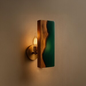 May include: A wall sconce featuring a wooden frame with a live edge design and a rectangular green resin inlay. The sconce has a brass-colored base and a vintage-style light bulb.