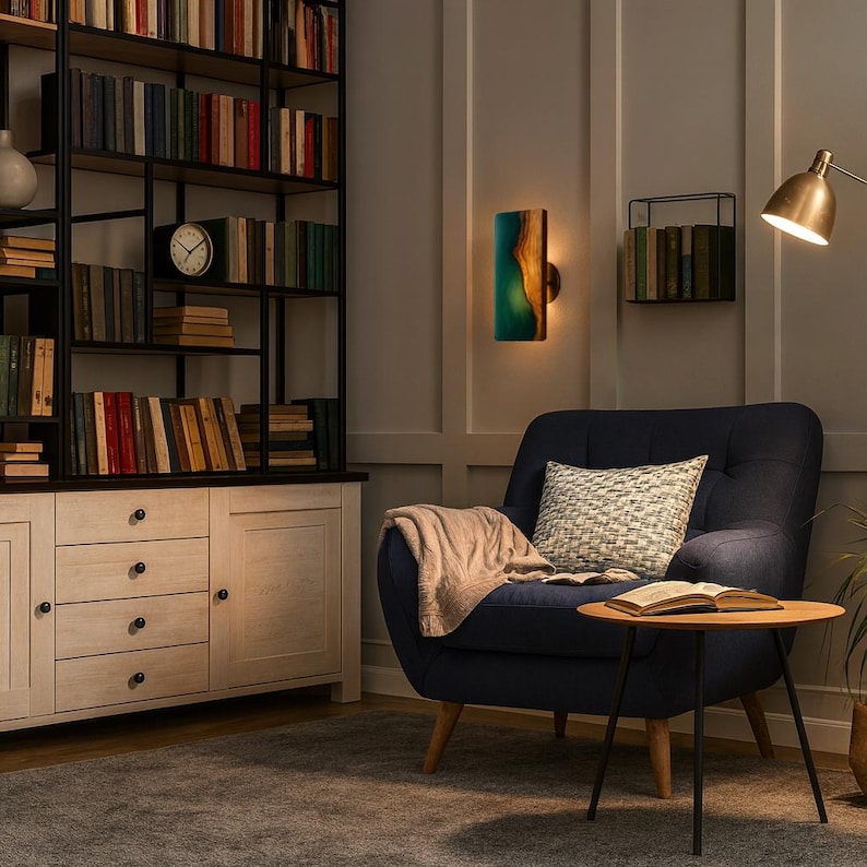 May include: A cozy reading nook featuring a navy blue armchair with a patterned pillow and a wooden side table. A wooden and resin wall sconce provides ambient lighting. A large bookshelf and a floor lamp complete the scene.