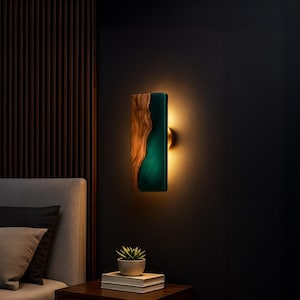 May include: A rectangular wall sconce with a wood and teal resin design. The wood grain is visible on the left side, while the right side features a teal resin. The sconce emits a warm glow, creating a modern and artistic lighting fixture.