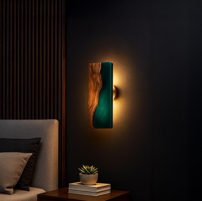May include: A rectangular wall sconce with a wood and teal resin design. The wood grain is visible on the left side, while the right side features a teal resin. The sconce emits a warm glow, creating a modern and artistic lighting fixture.
