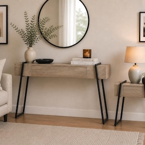 May include: A light wood console table and matching side table with black metal legs. A round mirror hangs above the console table. A lamp, vase, and framed art pieces decorate the room. The tables have drawers.