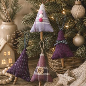 Könnte beinhalten: Handgefertigte Weihnachtsbaumschmuck in verschiedenen Lila- und Karomustern. Jeder Baum aus Stoff hat einzigartige Details wie Pompons, Knöpfe und Schleifen. Die Ornamente werden an einem Weihnachtsbaum präsentiert, mit einem Holzstern und einer Strickdecke.