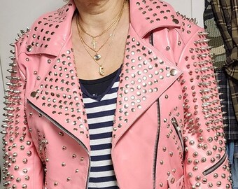 May include: A pink leather jacket with silver studs and spikes. The jacket has a zipper closure and a belt at the waist.