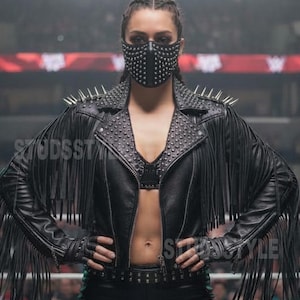 May include: Black leather jacket with fringe, studs, and spikes. The jacket has a cropped design and is paired with matching leather pants and a studded face mask. The outfit is worn in a wrestling ring setting.