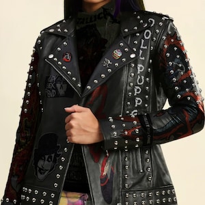 May include: A black leather jacket with silver studs and a colourful graphic print on the sleeves. The jacket has a zip closure and a collar. The text "JOL PUPPE" is printed on the back of the jacket.